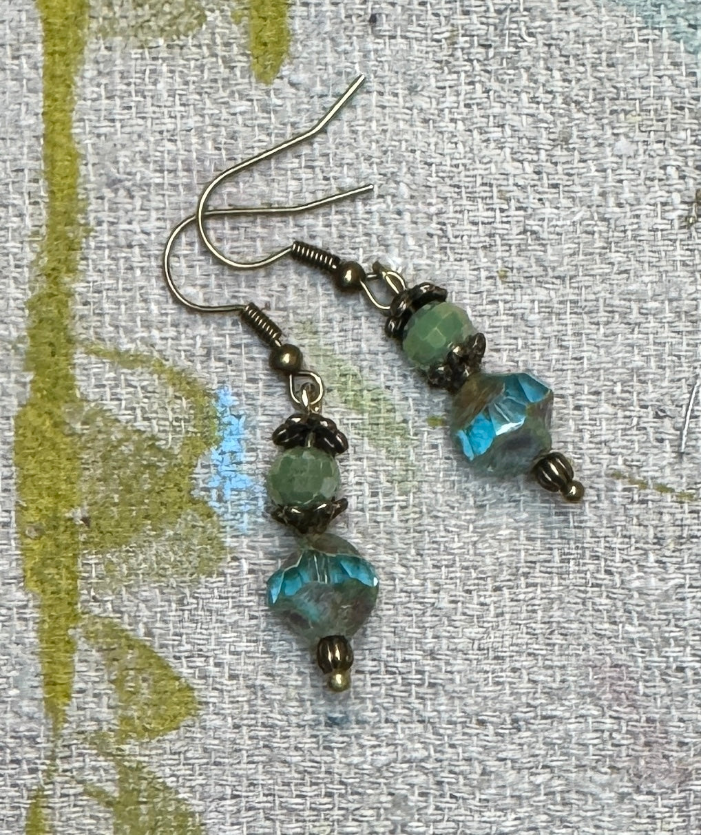 Misty Mornings handmade earrings featuring sage-green faceted Czech glass beads, weathered aqua-blue Saturn-shaped Czech glass beads, antique bronze floral bead caps, and bronze-tone fishhook earwires.