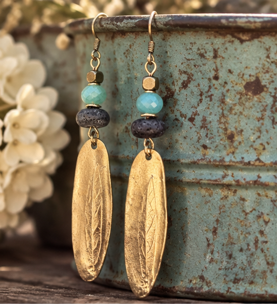 Golden Aqua Earrings by Patina Rabbit featuring handmade dark ceramic focal beads, soft aqua faceted Amazonite gemstones, and long textured gold Nunn Design pendants in a rustic artisan style. Hanging on a rustic old tin can.