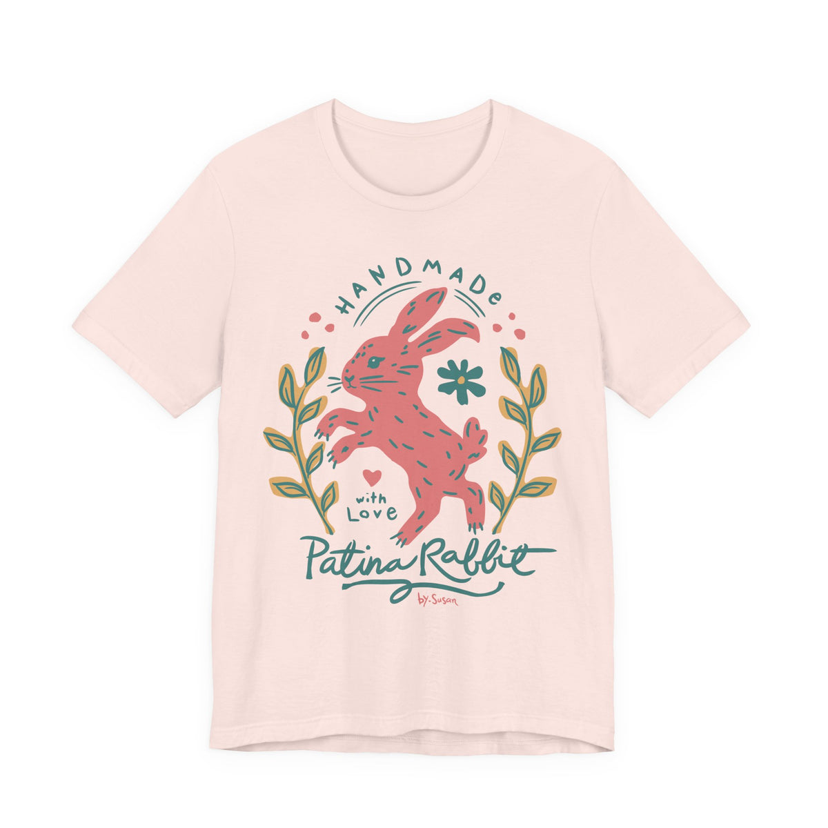 A soft pink t-shirt featuring a colorful graphic of a pink rabbit with the text 'HANDMADE with Love Patina Rabbit' and decorative leaves.