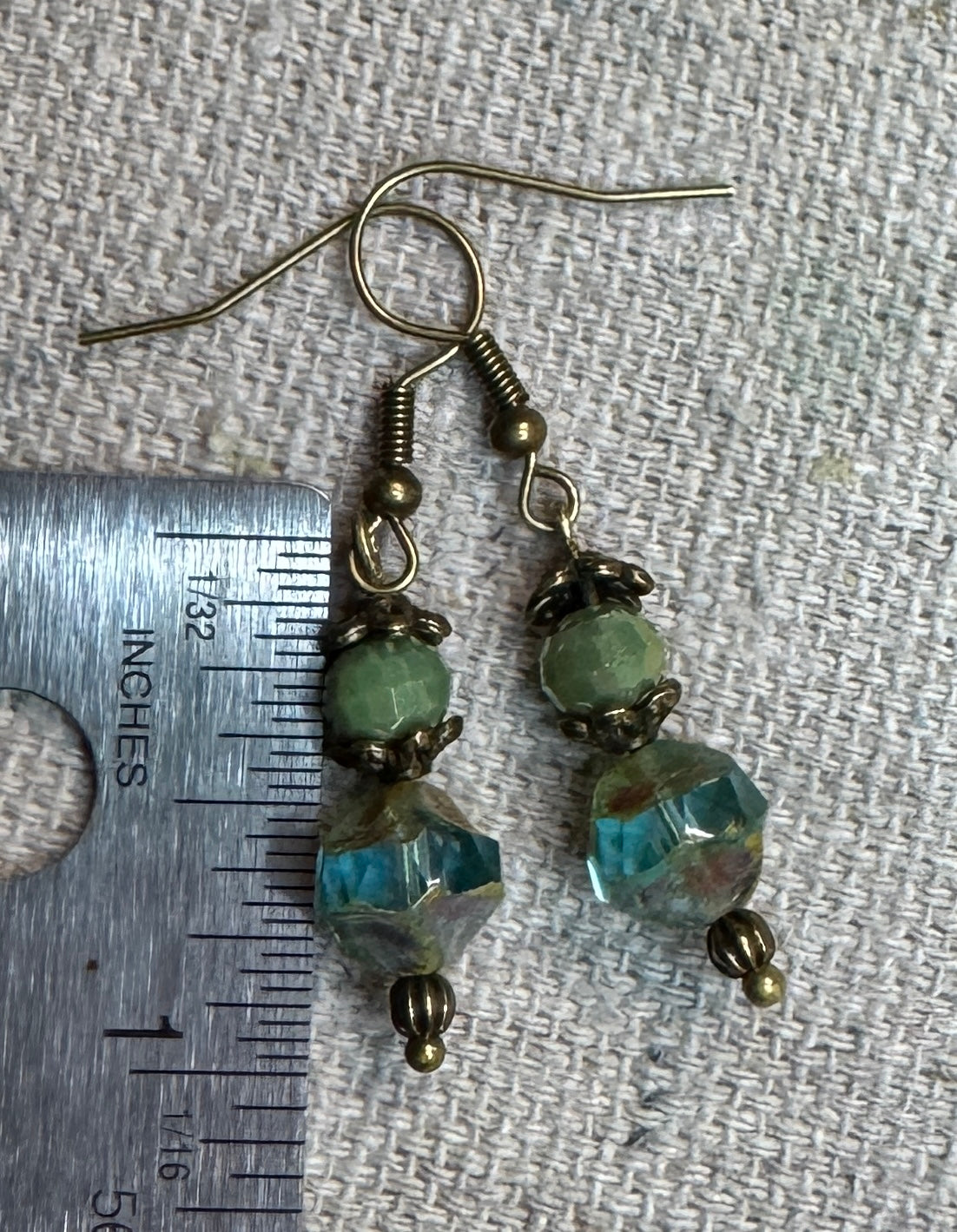 Misty Mornings handmade earrings featuring sage-green faceted Czech glass beads, weathered aqua-blue Saturn-shaped Czech glass beads, antique bronze floral bead caps, and bronze-tone fishhook earwires. beside a ruler showing earring will hang 1".