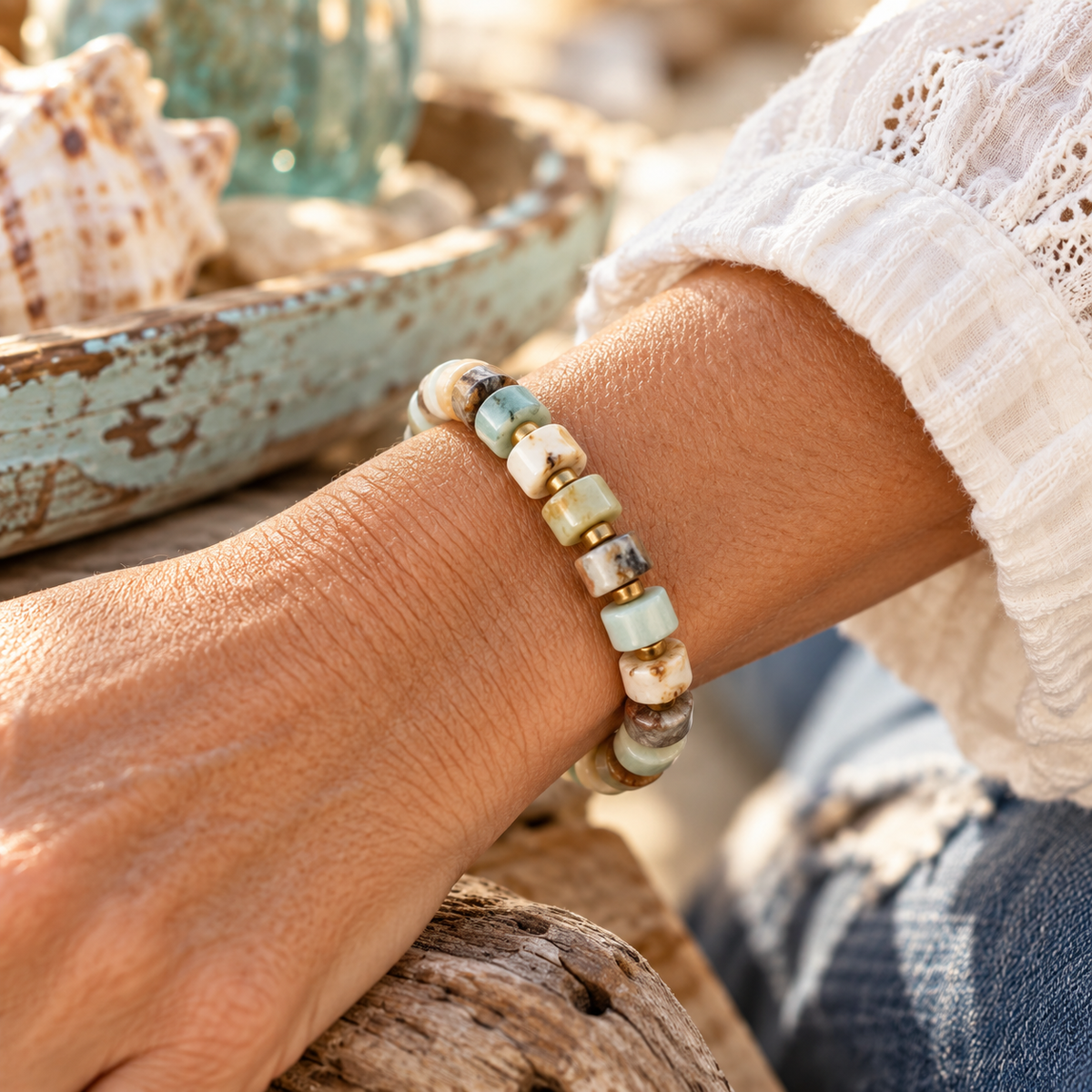 Woman wearing the Coastal Stone stretch bracelet, featuring 6mm Aqua Amazonite heishi beads in soft aqua, cream, gray and earthy tones with small gold seed bead accents.