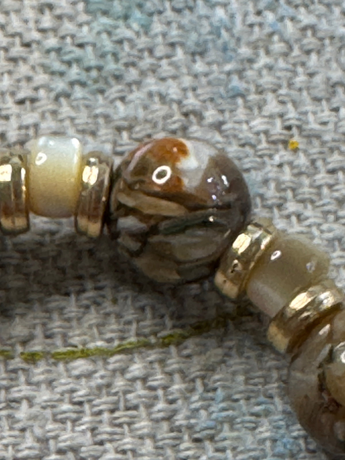 a close up view of a marbled brown lampwork beads, cream-colored spacer beads, and gold metal spacers